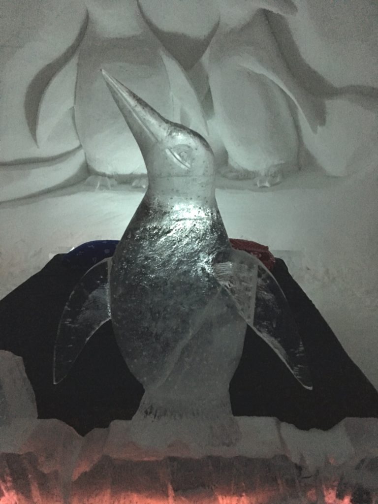 A solid ice penguin with ice sculpture in the background at the Snowhotel, Kirkenes, Finland